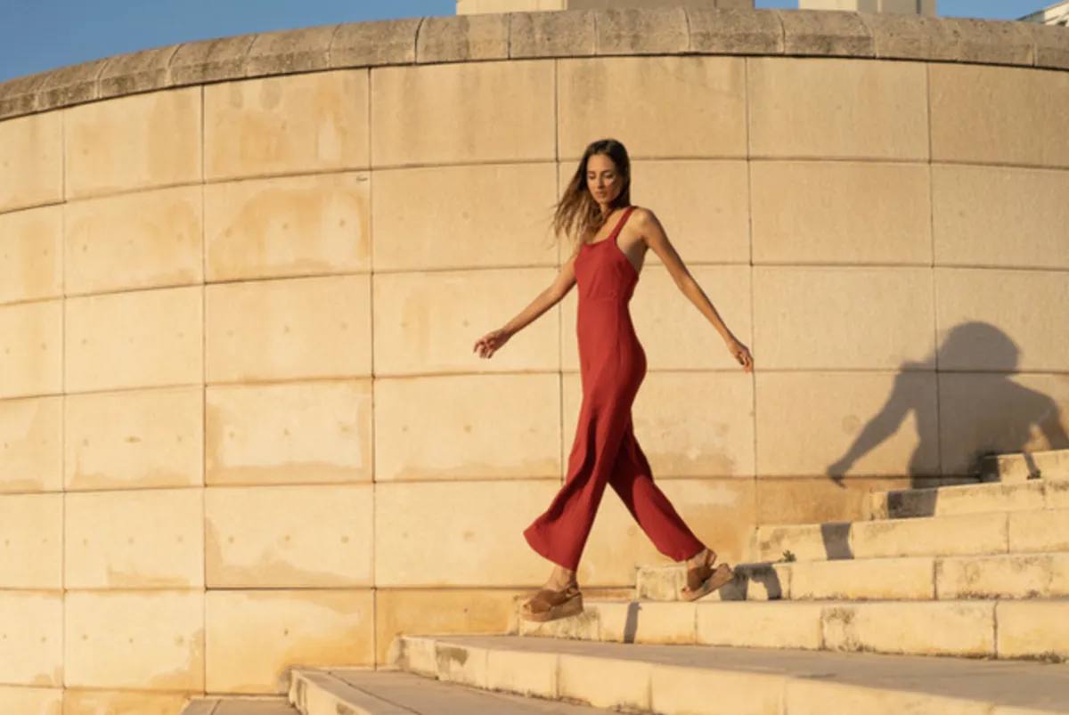 Full-length editorial model portfolio photo: model in a red jumpsuit walking down stone steps