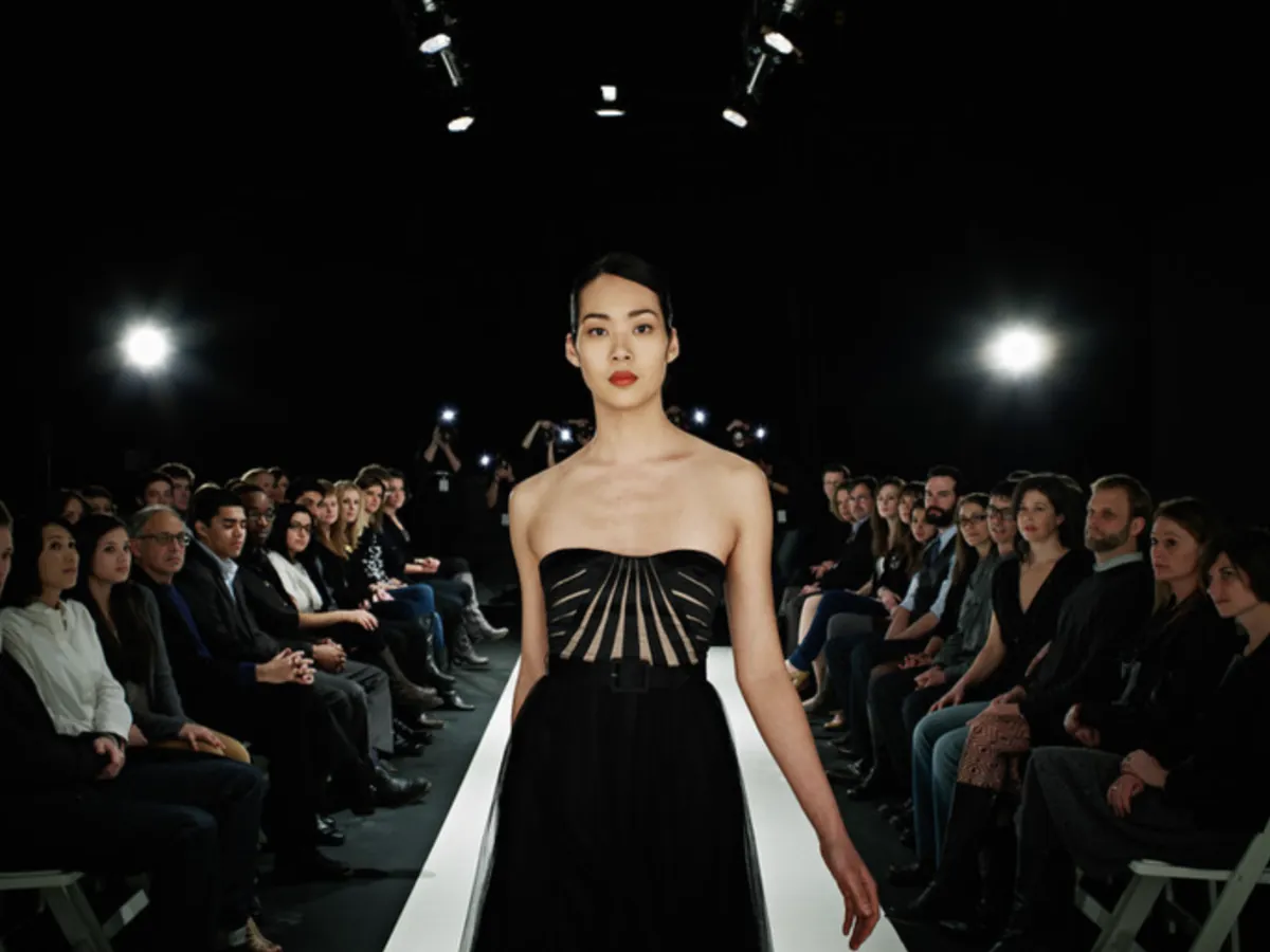 Runway model portfolio photo: model in a black gown on a lit catwalk