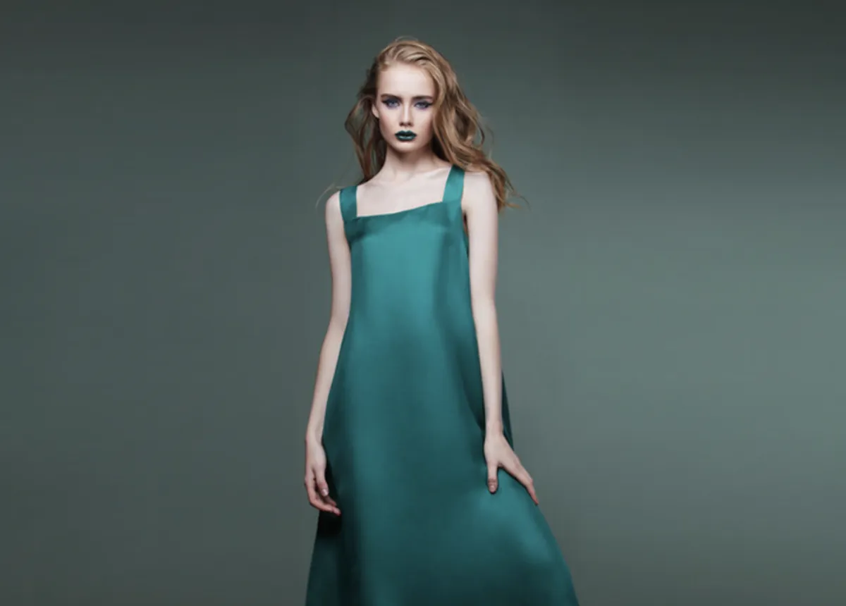 Studio fashion model portfolio photo: model in a teal satin slip dress on a grey backdrop