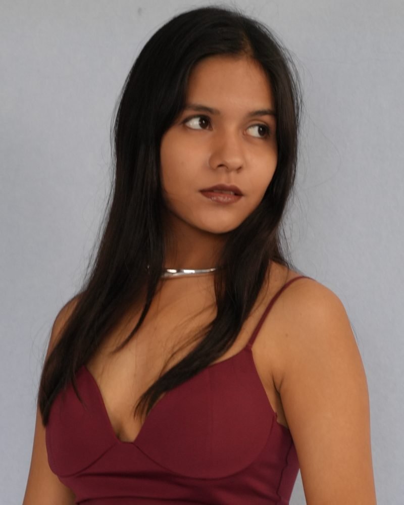 Commercial model in a burgundy dress and silver choker, studio portrait on a grey backdrop