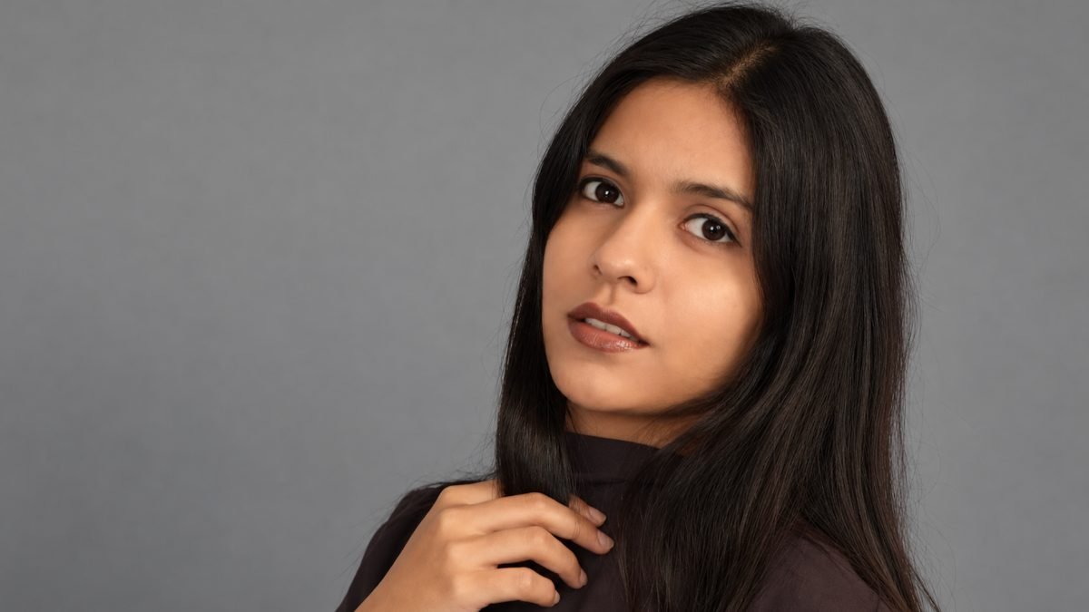 ZJELL model with long dark hair in a black high-neck top, studio portrait on a grey backdrop